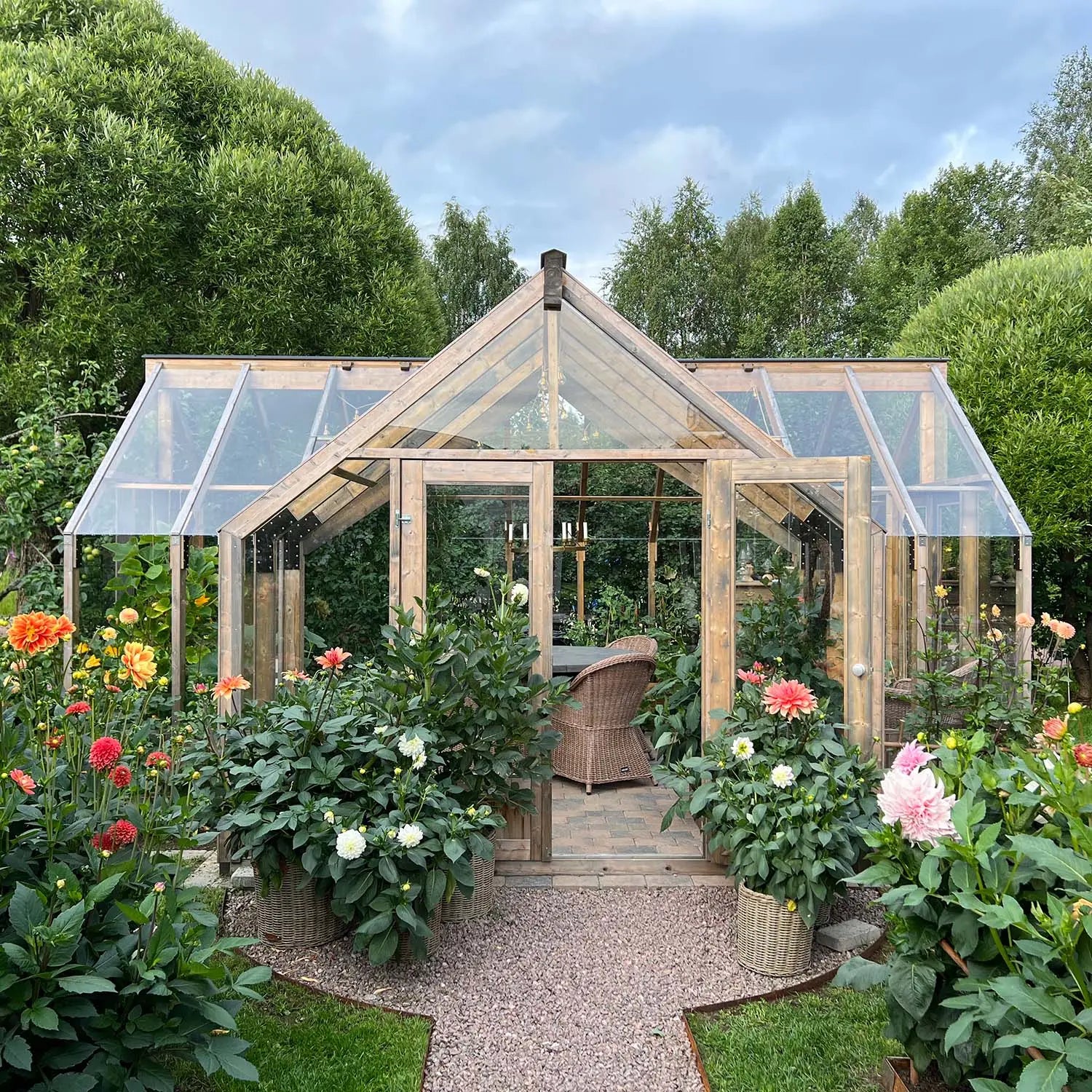 Wooden greenhouse with glass panels surrounded by flowers and greenery