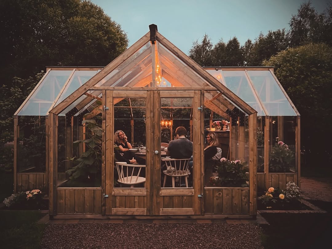 People sitting inside a wooden greenhouse with plants and tables.