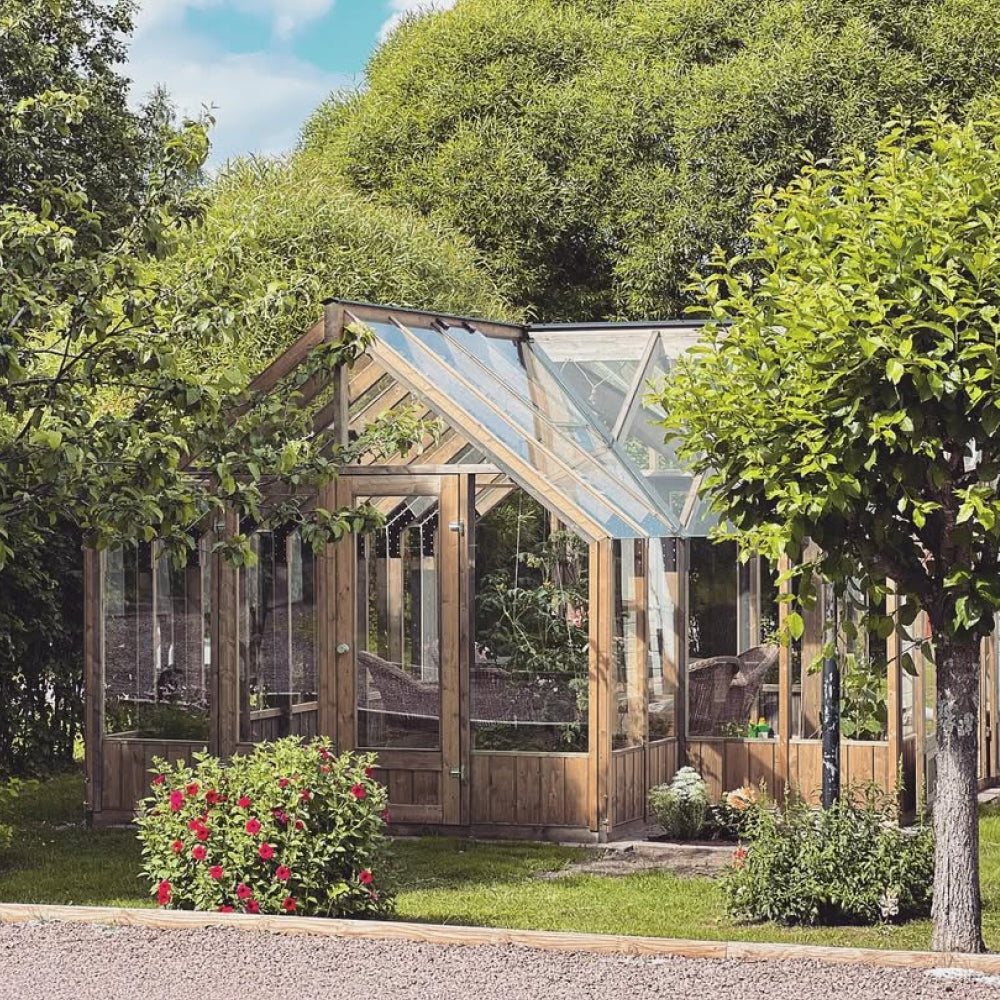 Wooden greenhouse with glass panels surrounded by greenery and flowers
