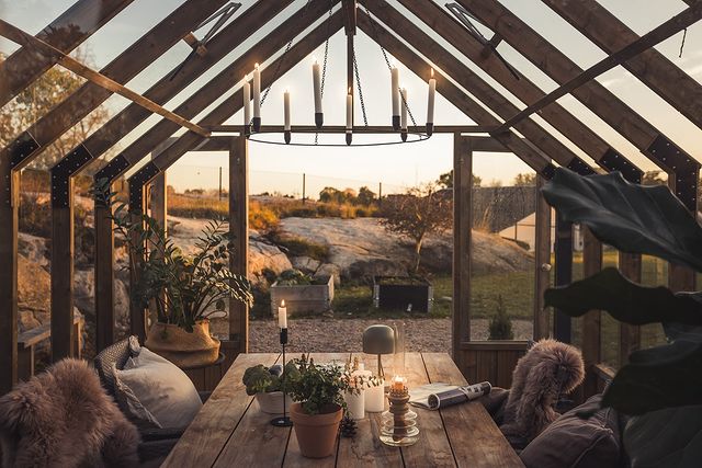 Cozy indoor setting with wooden beams, a table with candles and plants, and a scenic outdoor view.