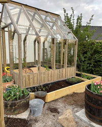 Wooden greenhouse with plants and gardening tools in a garden setting