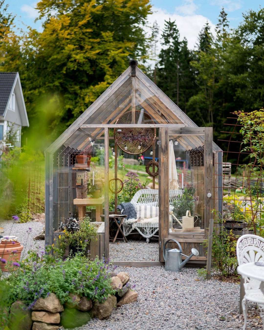 Wooden greenhouse in a garden with outdoor furniture and plants