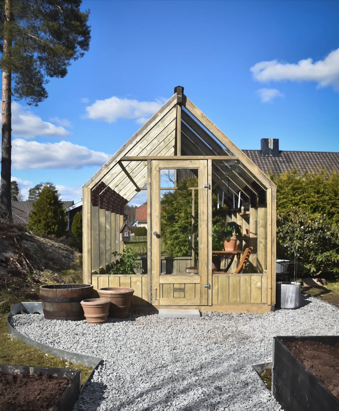 Wooden shed with glass doors in a garden setting under a blue sky.