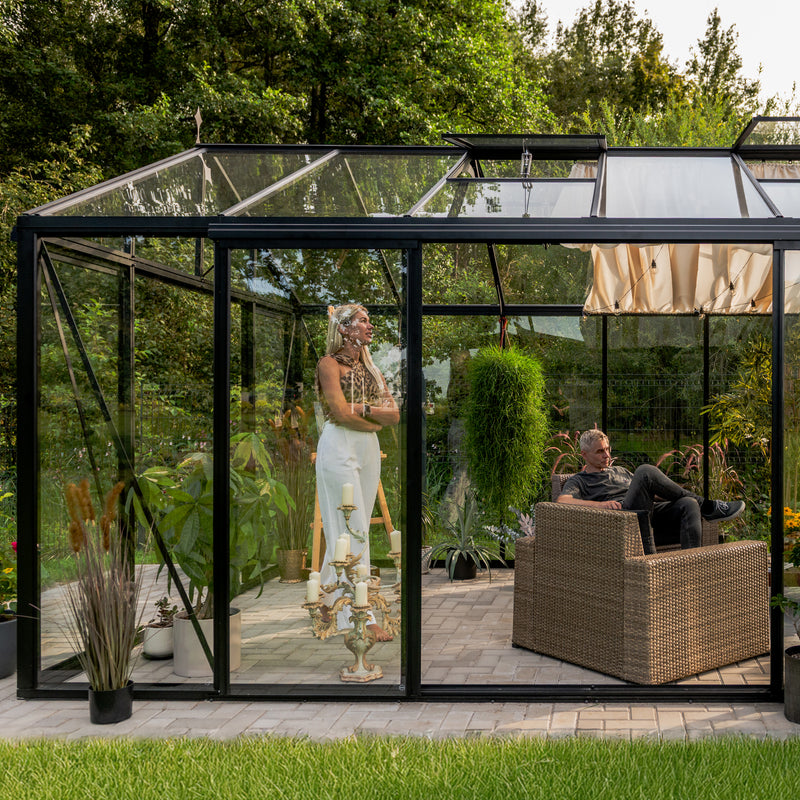 Inside a Scandiglass greenhouse at sunset - a woman reading in a lounge setting among plants.