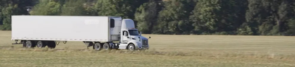 White semi truck with a freight trailer driving past a field