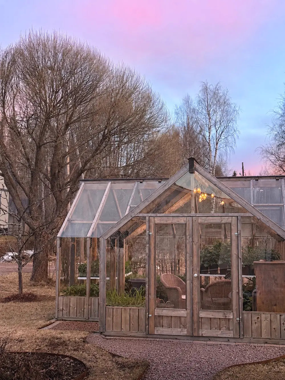 Greenhouse lit from inside under a pink dusk sky
