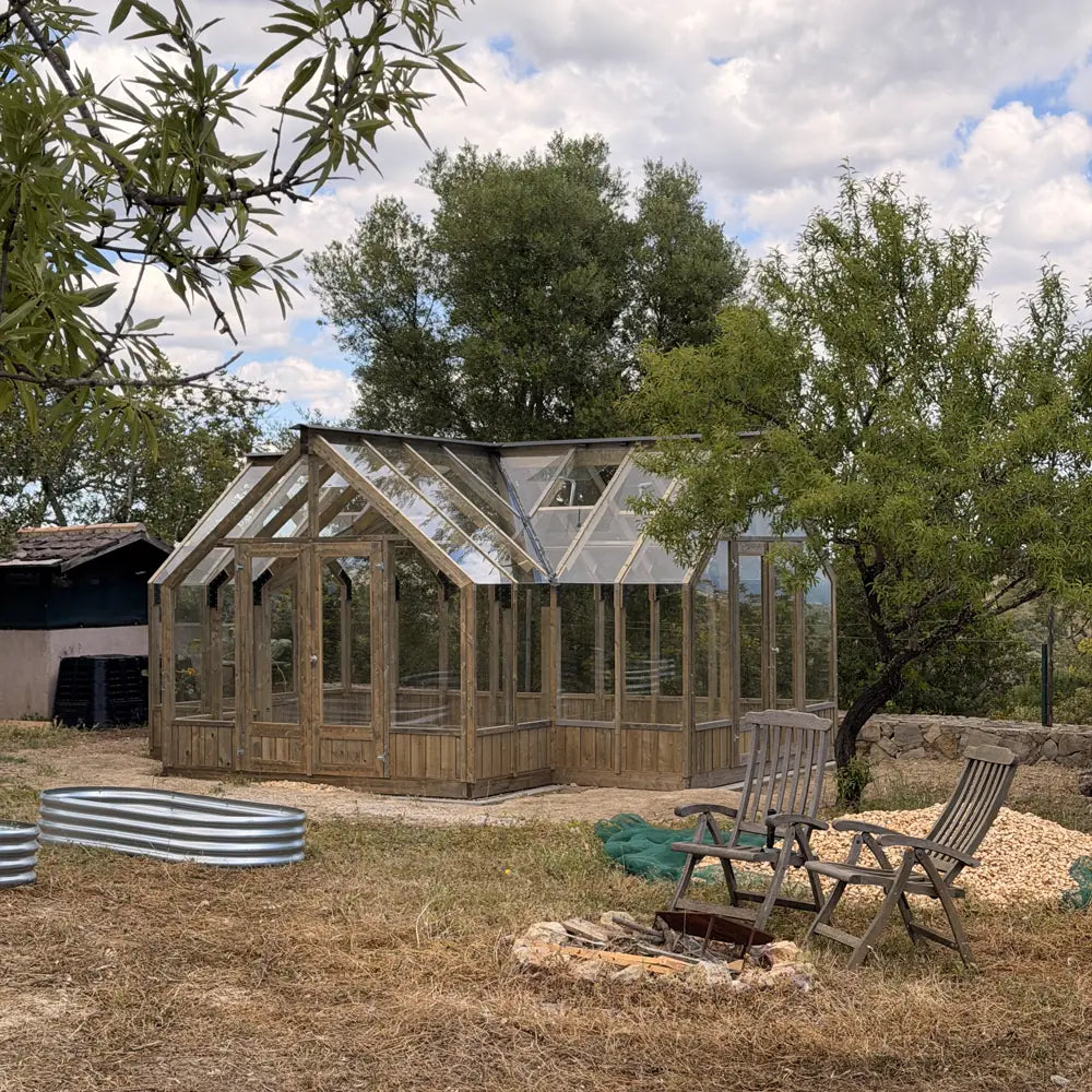 Greenhouse beside raised metal beds and a seating area